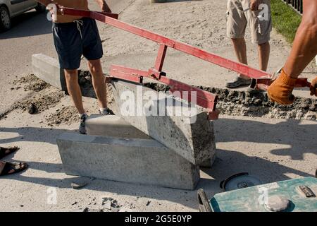 Der Prozess der Verlegung der Bürgersteig-Bordsteinkante. Die Arbeiter legen ein abgelenktes Stück Beton in eine vorbereitete Aussparung oder einen Graben. Stockfoto