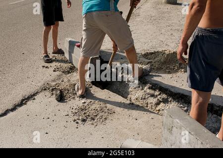 Der Prozess der Verlegung der Bürgersteig-Bordsteinkante. Die Arbeiter legen ein abgelenktes Stück Beton in eine vorbereitete Aussparung oder einen Graben. Stockfoto