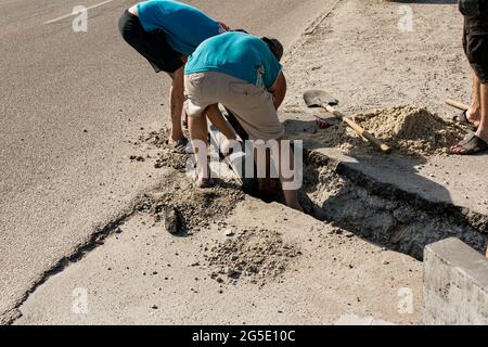 Der Prozess der Verlegung der Bürgersteig-Bordsteinkante. Die Arbeiter legen ein abgelenktes Stück Beton in eine vorbereitete Aussparung oder einen Graben. Stockfoto