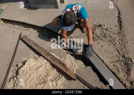 Der Prozess der Verlegung der Bürgersteig-Bordsteinkante. Die Arbeiter bereiten einen Graben für die Platzierung eines Betonklotz vor. Stockfoto