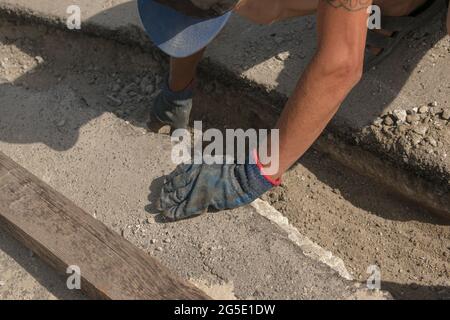 Der Prozess der Verlegung der Bürgersteig-Bordsteinkante. Die Arbeiter bereiten einen Graben für die Platzierung eines Betonklotz vor. Stockfoto