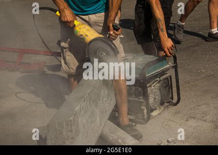 Der Prozess der Verlegung Bürgersteig Bordsteinkante. Ein Arbeiter schneidet einen Betonblock mit einer Kreissäge. Viel Staub. Stockfoto