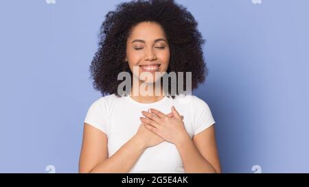 Glückliche afroamerikanische Frau fühlt dankbare Hände auf der Brust Stockfoto