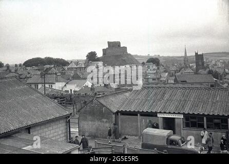 1960er Jahre, historisches Bild mit Luftaufnahme über den Launceston-Viehmarkt, Launceston, Cornwall, England, Großbritannien, mit dem Auktionsbüro im Vordergrund und dem alten Berghof und Turm des Launceston-Schlosses im Hintergrund. Der Turm der Magdalenenkirche von S. Maria ist auf der Rückseite rechts zu sehen. Stockfoto