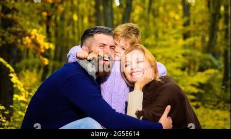 Eltern und Kind gemeinsam im Park am sonnigen Herbsttag. Glückliche Familie, Mutter und Vater umarmen den kleinen Sohn. Glückliches Paar mit Kind im Freien. Stockfoto