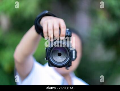 Der asiatische Mann hält die Mittelformatkamera in der Hand und fokussiert, um vor ihm zu fotografieren. Stockfoto