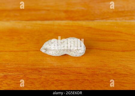 Erdnüsse auf einem Holztisch. Eine Erdnuss wird auf einem Holztisch mit Blick auf die Holzmaserung platziert. Stockfoto