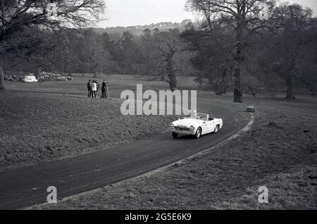 60er Jahre, historischer, oben offener MG Midget-Motorwagen, der eine Kurve auf einer ländlichen rmotorischen Rennstrecke umgeht, England, Großbritannien. Beachten Sie den Solidaritätsstrohballen an der Ecke. Der kleine zweisitzige Sportwagen MG Midget wurde von MG von 1961 bis 1979 hergestellt, ursprünglich auf Basis des Austin-Healey Sprite. Stockfoto