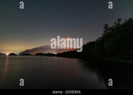 Ein Blick auf den Nachthimmel über dem Derwent-Wasser im englischen Lake District mit dem orangefarbenen Leuchten von Keswick Stockfoto