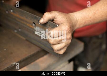 Gebohrte Löcher in das Metall. Arbeiten Sie in einer Metallwerkstatt. Die Hand hält einen Stahlrohling. Ein Mann arbeitet in der Garage. Stockfoto