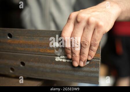 Gebohrte Löcher in das Metall. Arbeiten Sie in einer Metallwerkstatt. Die Hand hält einen Stahlrohling. Ein Mann arbeitet in der Garage. Stockfoto