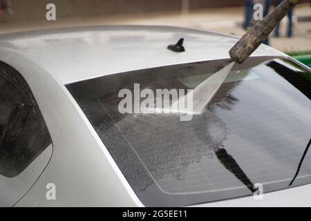 Autowäsche. Das Auto wird unter dem Druck eines Wasserstrahls gewaschen. Mit einem Wasserspray Schmutz von der Fahrzeugoberfläche abwaschen. Stockfoto