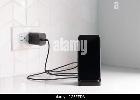 Ein schwarzes Smartphone, das an eine kabellose Ladestation angeschlossen ist und an eine weiße Küchentischplatte oder Bank mit Kopierplatz angeschlossen ist Stockfoto