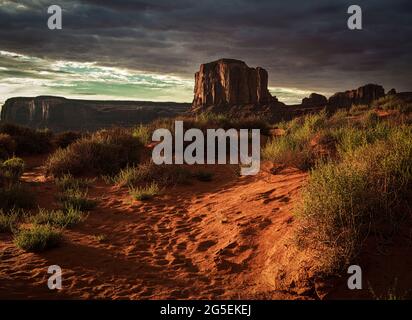 Wunderschöner Sonnenuntergang in Monument Valley Wüste bedeckt mit Sträuchern Stockfoto