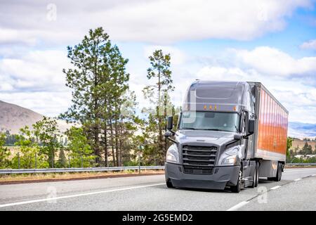 Grauer großer Langstrecken-Industrie-Sattelschlepper, der kommerzielle Fracht in einem trockenen Transporter transportiert und auf der Sommerautobahn zur Auslieferung läuft Stockfoto