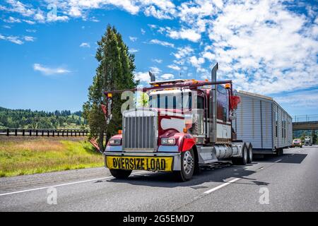 Speziell ausgestattete American Idol Red Classic Big Rig Semi-Truck mit Chromteilen und Übergröße Last Zeichen o das Dach transportiert Manufakturhaus auf Stockfoto