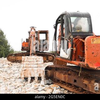 Orangefarbene rostige, abgenutzte Bulldozer-Bagger vor Ort, die am Nachmittag in einem kargen Land Bauarbeiten durchmachten Stockfoto