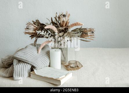 Stillleben im skandinavischen Stil mit einem Blumenstrauß, einem Strickelement und dekorativen Details. Stockfoto