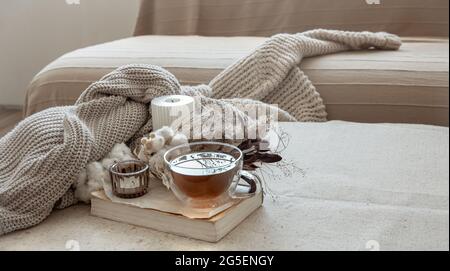 Glas-Tasse Tee, gestricktes Element und getrocknete Blumen im Innenraum des Zimmers. Stockfoto