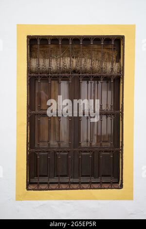 Ein Fenster mit metallenen Sicherheitsriegeln, die an einer weißen Wand in gelber Farbe eingerahmt sind Stockfoto