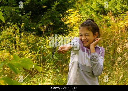 Lachendes Mädchen, das Vögel im Herbstwald füttert. Das Konzept, ein gemeinsames Familienwochenende in der Natur zu verbringen. Stockfoto