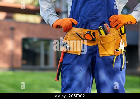 Männlicher Baumeister in blauen Overalls mit Werkzeuggürtel. Nahaufnahme des Hüftbereichs Stockfoto