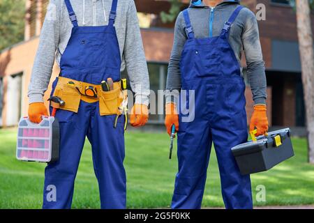 Ausgeschnittene Aufnahme von zwei männlichen Bauherren in blauen Overalls mit Werkzeugkasten auf der Baustelle Stockfoto