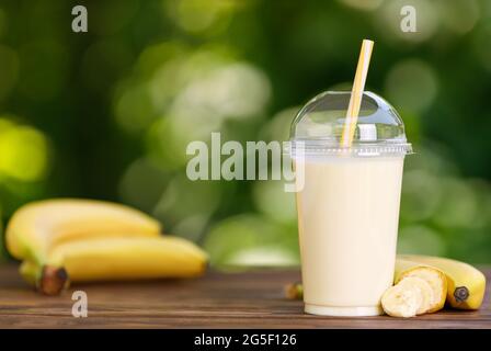 Bananenmilchshake in Einweg-Plastikglas auf Holztisch Stockfoto
