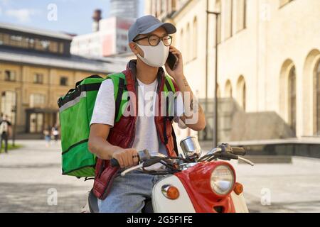 Junger asiatischer männlicher Kurier mit Thermosack, der Gesichtsschutz trägt Stockfoto