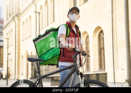 Junger asiatischer männlicher Kurier mit Thermosack, der Gesichtsschutz trägt Stockfoto