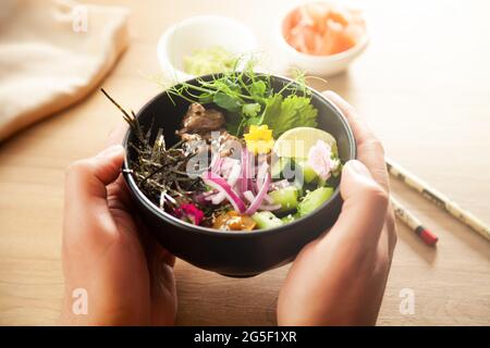 Ein Mann hält einen Poke-Salat mit Rindfleisch in einer Schüssel in den Händen. Zutaten Rindfleisch, Nameko-Pilze, Kirschtomaten, Reis, Gurke, Rote Zwiebel, Sesam Stockfoto