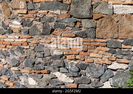 Textur einer Wand aus verschiedenen Steinen und Ziegeln. Die unregelmäßigen schwarzen und weißen Steine stehen im Kontrast zu den normalen roten Steinen. Stockfoto