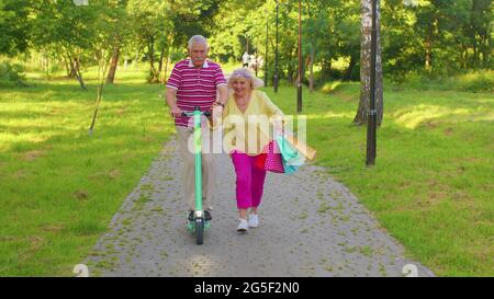 Ältere stilvolle Paar Großmutter, Großvater nach dem Einkaufen mit Taschen mit Roller zum Reiten Stockfoto