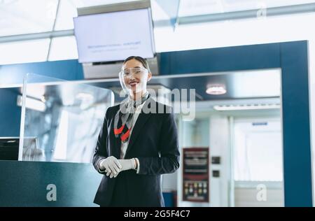 Bodenwächter mit Gesichtsschutz, der am Flughafen steht. Flughafenmitarbeiter während einer Pandemie warten auf Passagiere. Stockfoto