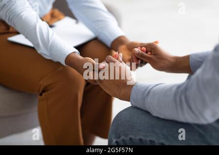 Professionelles Mitgefühl. Psychotherapeut unterstützt ihren depressiven männlichen Patienten, hält seine Hand in geschlossenen Räumen. Psychologe tröstet jungen Mann w Stockfoto