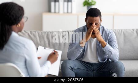 Verzweifelter schwarzer Mann, der an einem ernsten Zusammenbruch oder einer Depression leidet, Sitzung im Büro des Psychologen, Panorama. Gestresster männlicher Patient, Treffen w Stockfoto