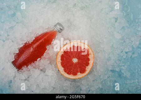 Nahaufnahme eine Glasflasche mit kaltem Saft-Cocktail-Getränk mit Chiasamen und halbgeschnittener rosa Grapefruit auf zerkleinertem Eis im Einzelhandel, erhöhter Hig Stockfoto