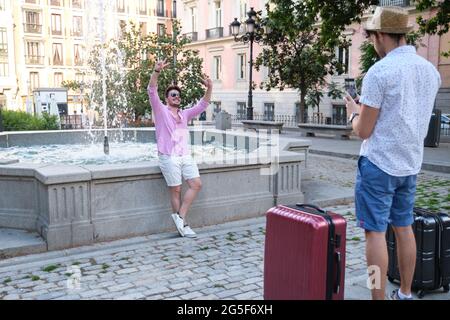 Mann, der am Brunnen auf einem Stadtplatz ein Foto seines glücklichen Freundes macht. Stockfoto