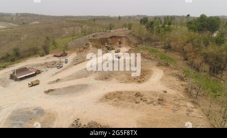 Bagger auf der Baustelle Schnitte Hill und Lasten Lkw mit Erde. Luftaufnahme schwere Maschinen bereitet die Landschaft für den Bau. Bagger werden in großen und kleinen Bauwerken, Indonesien Stockfoto
