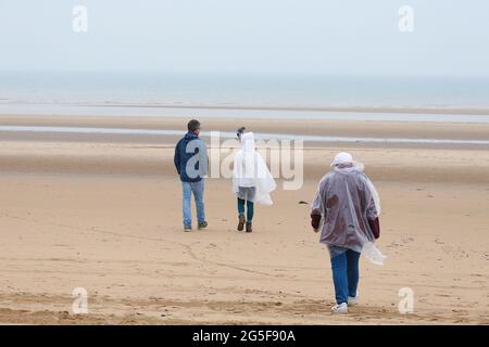 Camber, East Sussex, Großbritannien. 27 Juni 2021. Wetter in Großbritannien: Das später erwartete Regenwetter ist früh an den Sandstränden von Camber Sands in East Sussex angekommen. Einige Familien wollen den Tag genießen, wenn sie mit Regenschirmen und Regenponchos ankommen. Foto-Kredit: Paul Lawrenson /Alamy Live Nachrichten Stockfoto