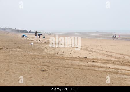 Camber, East Sussex, Großbritannien. 27 Juni 2021. Wetter in Großbritannien: Das später erwartete Regenwetter ist früh an den Sandstränden von Camber Sands in East Sussex angekommen. Einige Familien wollen den Tag genießen, wenn sie mit Regenschirmen und Regenponchos ankommen. Foto-Kredit: Paul Lawrenson /Alamy Live Nachrichten Stockfoto