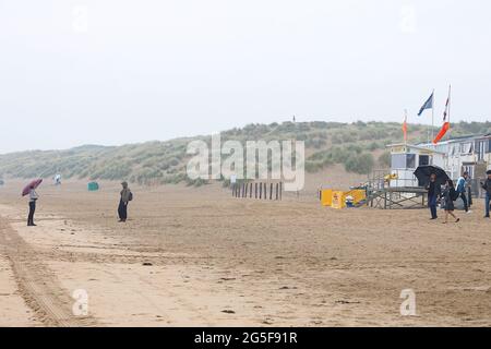 Camber, East Sussex, Großbritannien. 27 Juni 2021. Wetter in Großbritannien: Das später erwartete Regenwetter ist früh an den Sandstränden von Camber Sands in East Sussex angekommen. Einige Familien wollen den Tag genießen, wenn sie mit Regenschirmen und Regenponchos ankommen. Foto-Kredit: Paul Lawrenson /Alamy Live Nachrichten Stockfoto