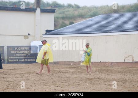 Camber, East Sussex, Großbritannien. 27 Juni 2021. Wetter in Großbritannien: Das später erwartete Regenwetter ist früh an den Sandstränden von Camber Sands in East Sussex angekommen. Einige Familien wollen den Tag genießen, wenn sie mit Regenschirmen und Regenponchos ankommen. Foto-Kredit: Paul Lawrenson /Alamy Live Nachrichten Stockfoto