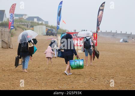 Camber, East Sussex, Großbritannien. 27 Juni 2021. Wetter in Großbritannien: Das später erwartete Regenwetter ist früh an den Sandstränden von Camber Sands in East Sussex angekommen. Einige Familien wollen den Tag genießen, wenn sie mit Regenschirmen und Regenponchos ankommen. Foto-Kredit: Paul Lawrenson /Alamy Live Nachrichten Stockfoto