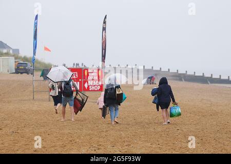 Camber, East Sussex, Großbritannien. 27 Juni 2021. Wetter in Großbritannien: Das später erwartete Regenwetter ist früh an den Sandstränden von Camber Sands in East Sussex angekommen. Einige Familien wollen den Tag genießen, wenn sie mit Regenschirmen und Regenponchos ankommen. Foto-Kredit: Paul Lawrenson /Alamy Live Nachrichten Stockfoto