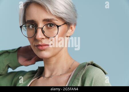 Kaukasische schöne silberne Mädchen posiert in Brillen auf Kamera isoliert auf blauem Hintergrund Stockfoto