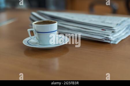 Ein Glas türkischen Kaffees auf einem Holztisch mit einem Stapel Zeitungen Stockfoto