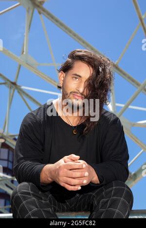 Porträt eines jungen Mannes, der in einem Skatepark sitzt und eine akrobatische Straßentänzerin mit langen Haaren ist. Stockfoto
