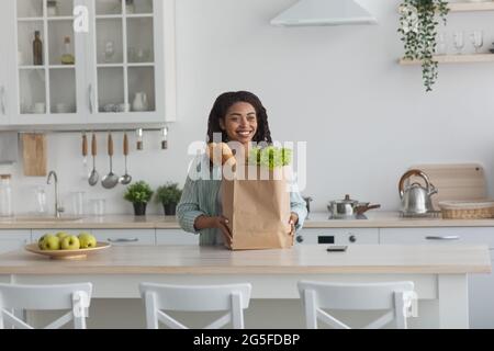 Lebensmitteleinkäufe, Lebensmittel aus dem Supermarkt bestellen und nach Hause liefern, neu normal. Fröhliche junge afroamerikanische Frau mit Öko-Tasche aus dem Geschäft mit vege Stockfoto
