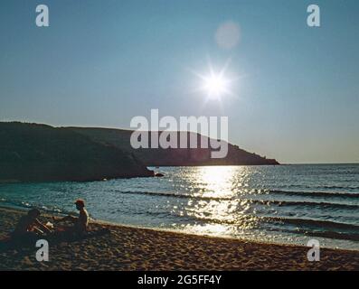 Gescanntes Bild einer unspezifischen Strandszene, kleine Familie mit Hintergrundbeleuchtung am Meeresrand in Griechenland, Starburst-Sonne am Himmel. Alles ist ruhig. Stockfoto